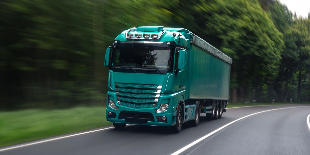 Green semi-truck speeding on a forest-lined road.