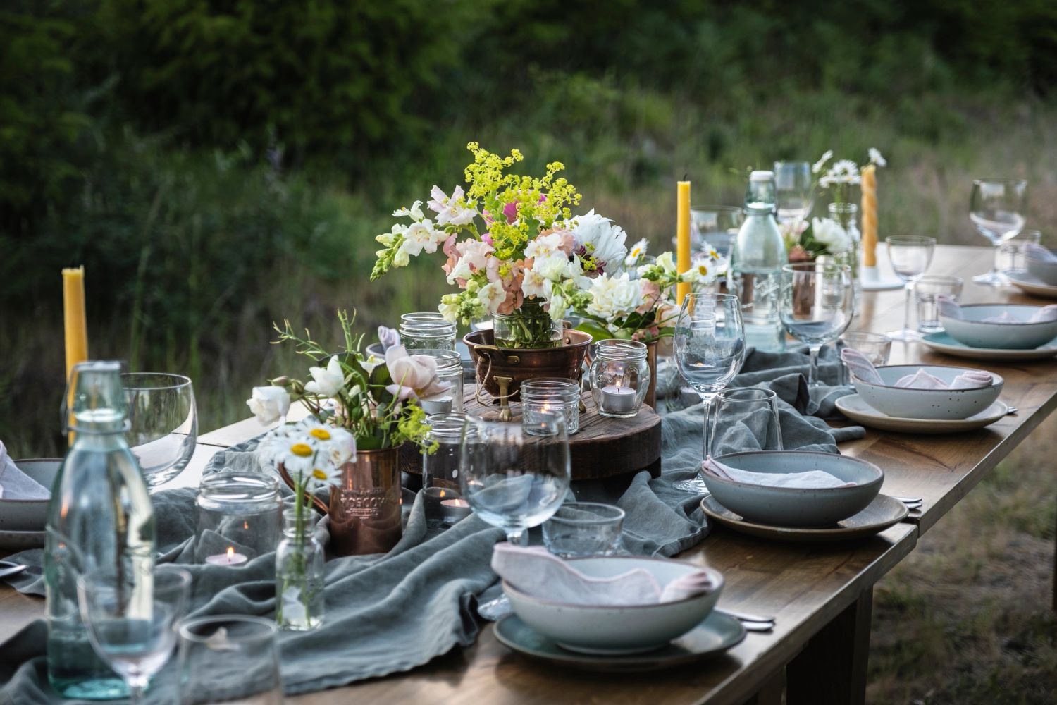 Elegant outdoor dining table with flowers, candles, and glassware.