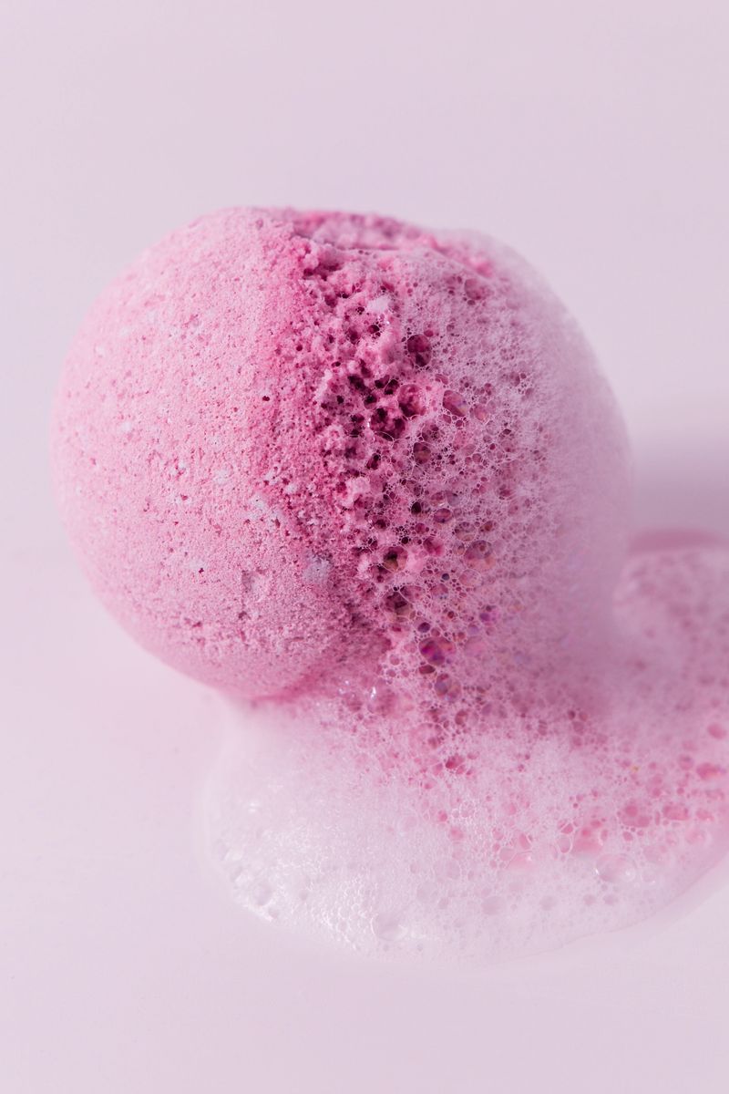 A vibrant pink bath bomb dissolves in water creating a frothy bubbly effect that enhances relaxation in a bath setting.