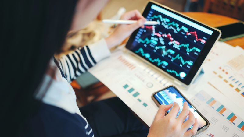 young asian woman sits outdoors using a tablet to AI track financial data, cryptocurrency prices, and stock investments via a fintech app. the video captures the modern habits of gen z investors who rely on mobile platforms and technology-driven tools to manage portfolios and build financial independence.