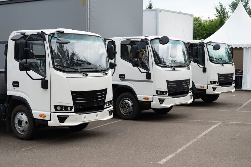 Three modern white delivery trucks aligned in a parking area, surrounded by a neutral backdrop. Concept of logistics and transport
