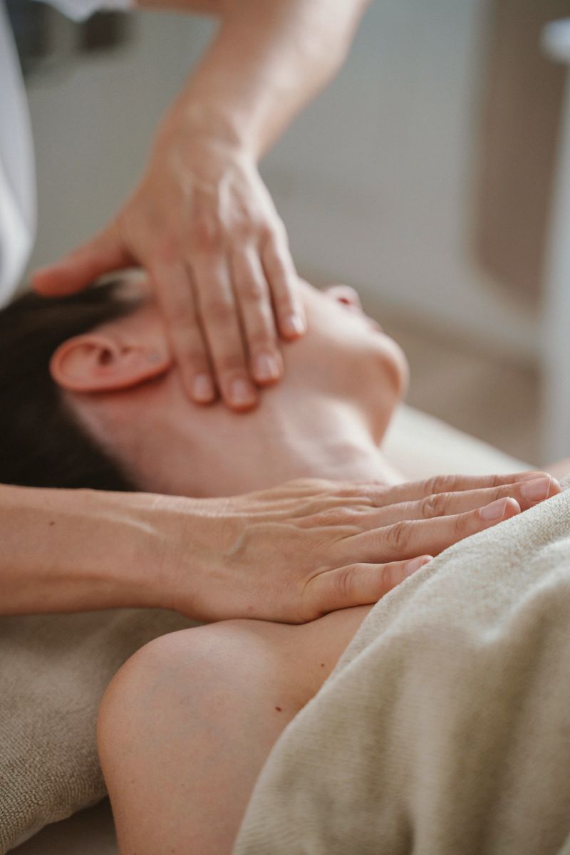 A person receives a soothing neck massage, relaxing on a comfortable surface under a soft towel. The hands applying the massage convey a sense of calm and relief