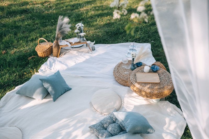 A charming picnic arrangement features soft cushions, wicker baskets, and decorative items on fresh green grass.