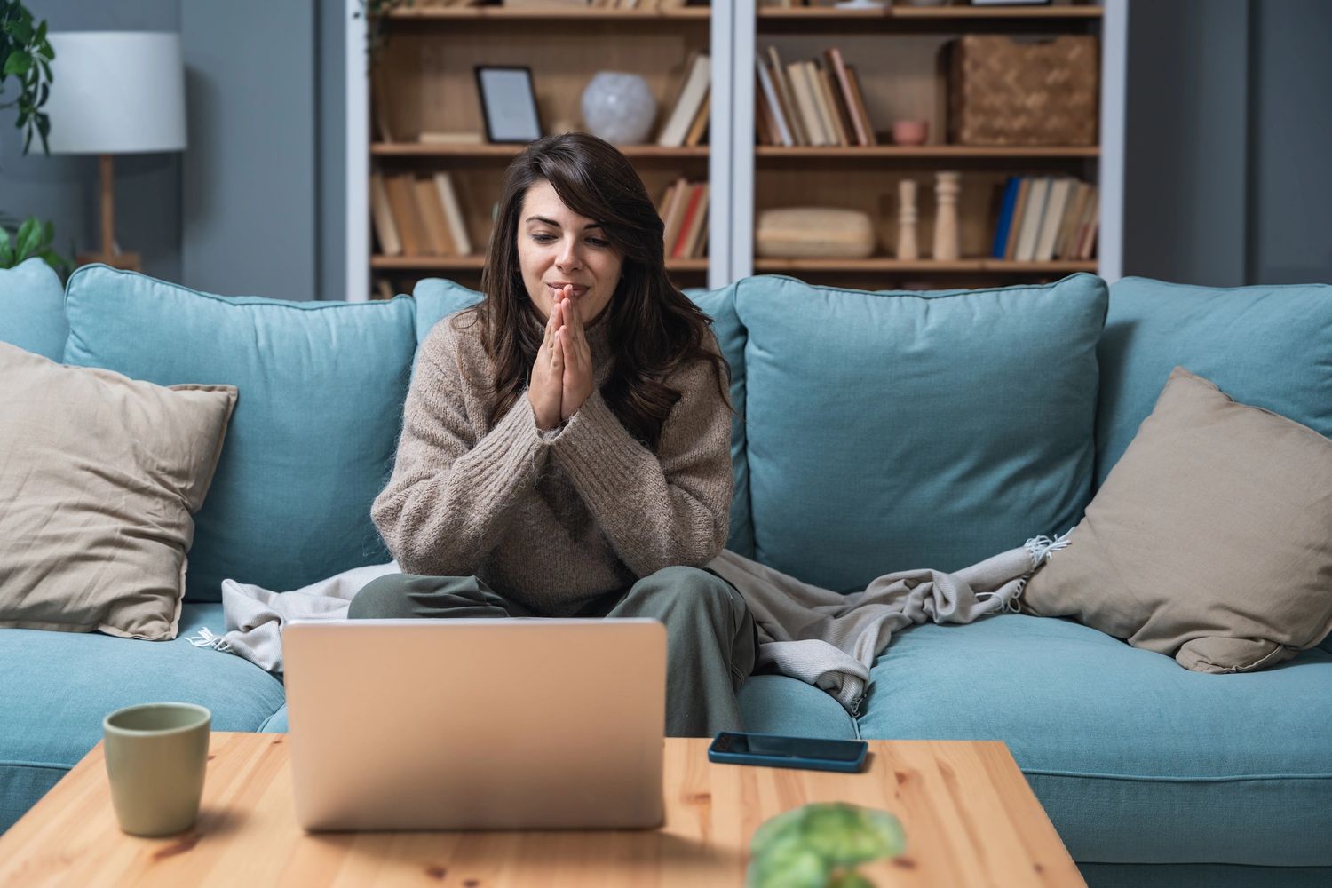 Woman sitting on a couch using a laptop, looking thoughtful.