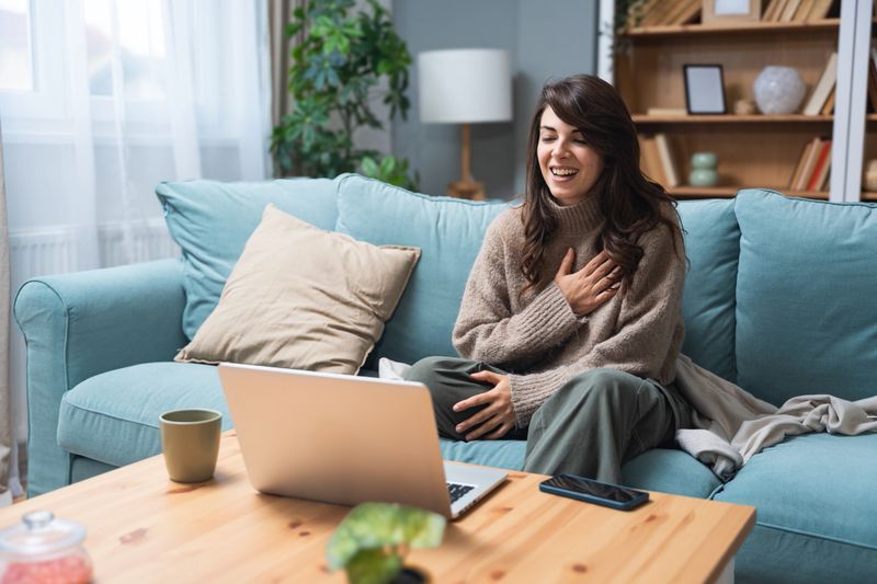Young woman attending online therapy session from her living room, expressing emotion while talking to a professional therapist, mental health and personal growth support via digital communication.