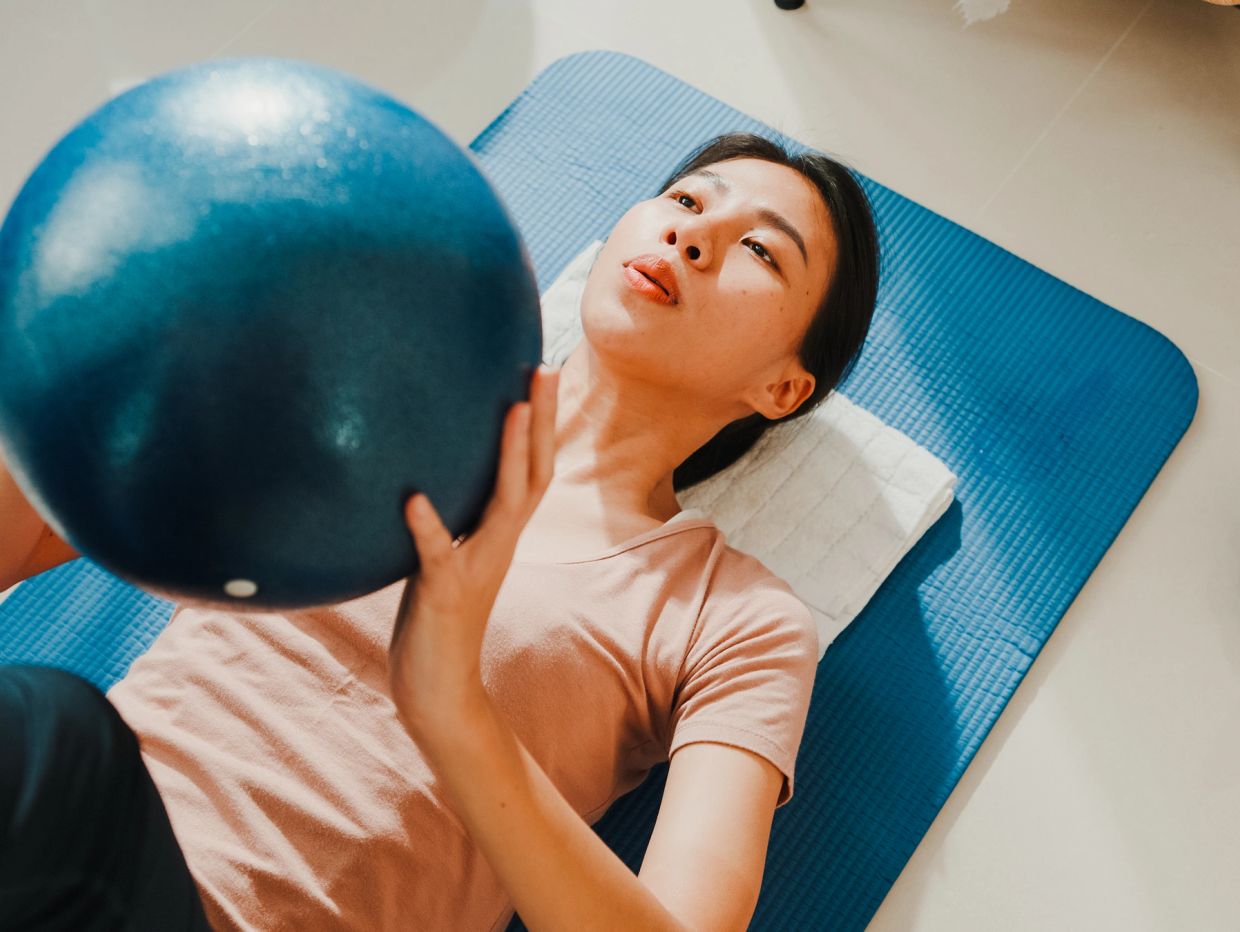 Woman exercising with a blue medicine ball on a yoga mat.