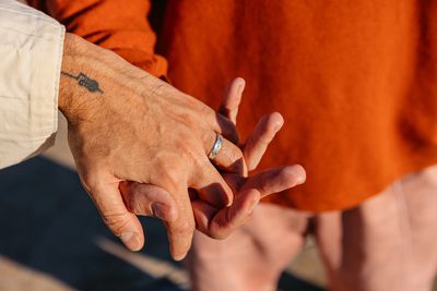 Two people holding hands with a visible tattoo and ring.