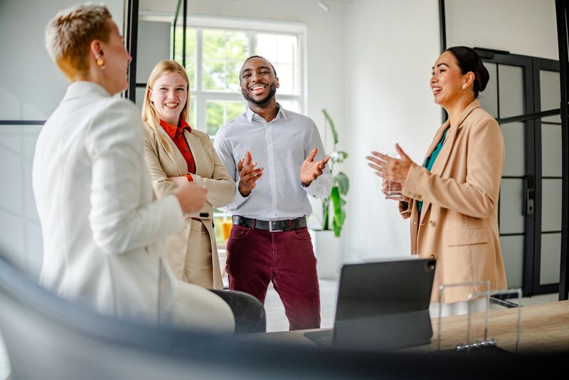 In a contemporary office, a young black man engages with his diverse team, encouraging discussion and collaboration while showcasing leadership and confidence in their professional setting.