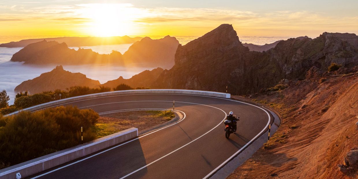Motorcyclist rides on mountain road at sunset.