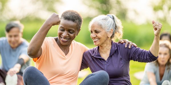 Two women celebrating fitness success outdoors in a group exercise session.