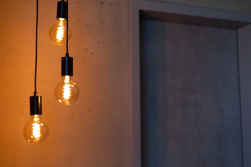 Three stylish pendant lights emit a warm glow in a contemporary setting. The soft illumination highlights the minimalist design of the space, creating a cozy atmosphere.