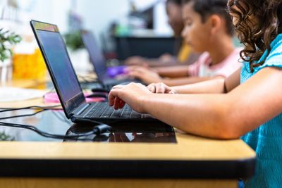 Children focused on typing on laptops in a classroom setting.