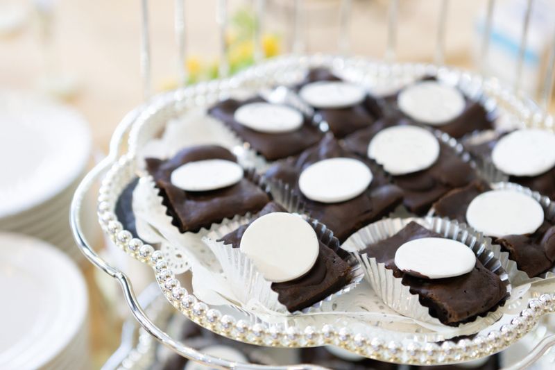 Elegant chocolate brownies with white fondant topping on a silver tray, perfect for luxury dessert catering or wedding reception