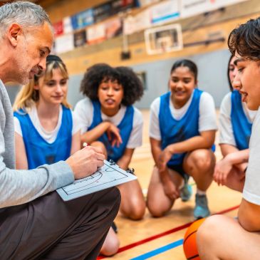 Coach discussing basketball strategy with young female players in a gym.