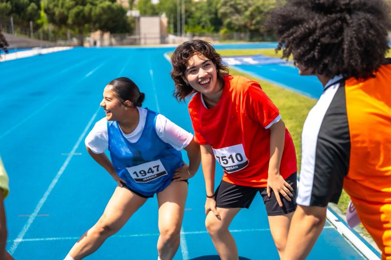 Teen athletes stretching together before a track race, getting ready to compete on a sunny day