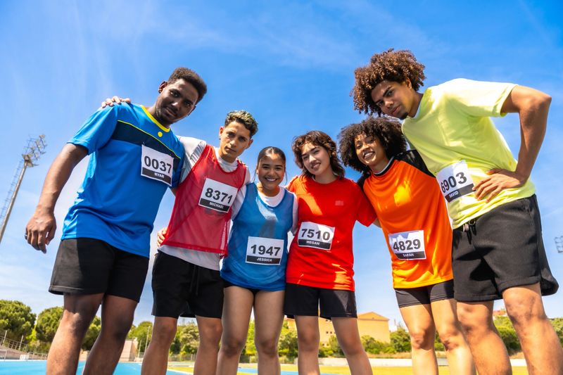 Group of young athletes smiling together before a track race, showing teamwork and sportsmanship