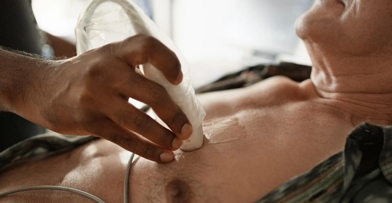 Close-up of doctor hand using ultrasound transducer to examine senior man's heart in medical clinic