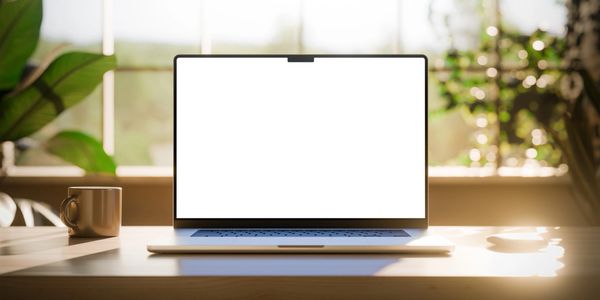 Laptop with blank screen on a wooden desk in bright natural light.