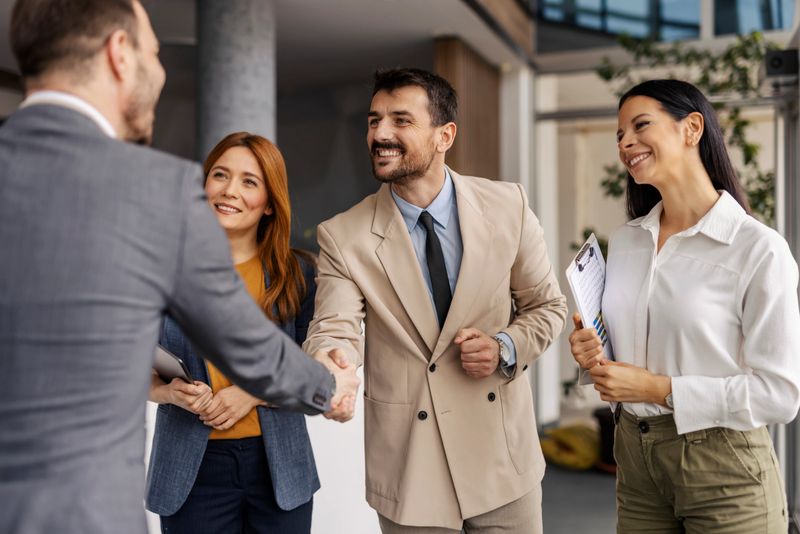 Businessmen shaking hands and greeting while female managers standing and smiling at them.