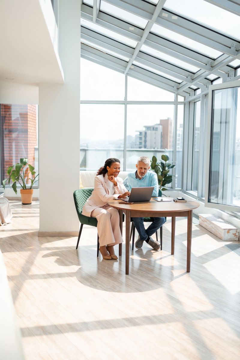 A professional man and woman working together on a laptop in a brightly lit modern office, symbolizing teamwork, collaboration, and contemporary work environments.