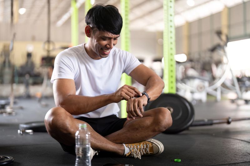 Athletic male sitting on gym floor, monitoring fitness progress with smartwatch. Concept of health and fitness tracking.