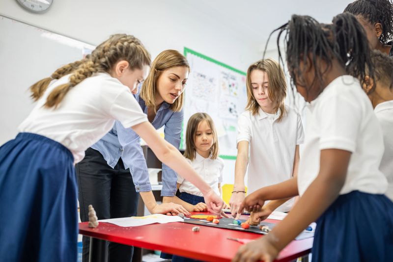 A diverse group of school children work together with their teacher on a hands-on educational project in a bright classroom.