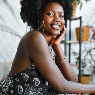 Smiling woman with natural hair in a patterned dress, posing indoors.