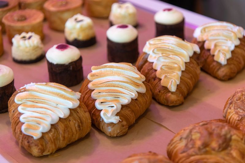 A variety of pastries and desserts are beautifully arranged on a display table. The treats include croissants topped with icing alongside small cakes, showcasing tempting flavors.