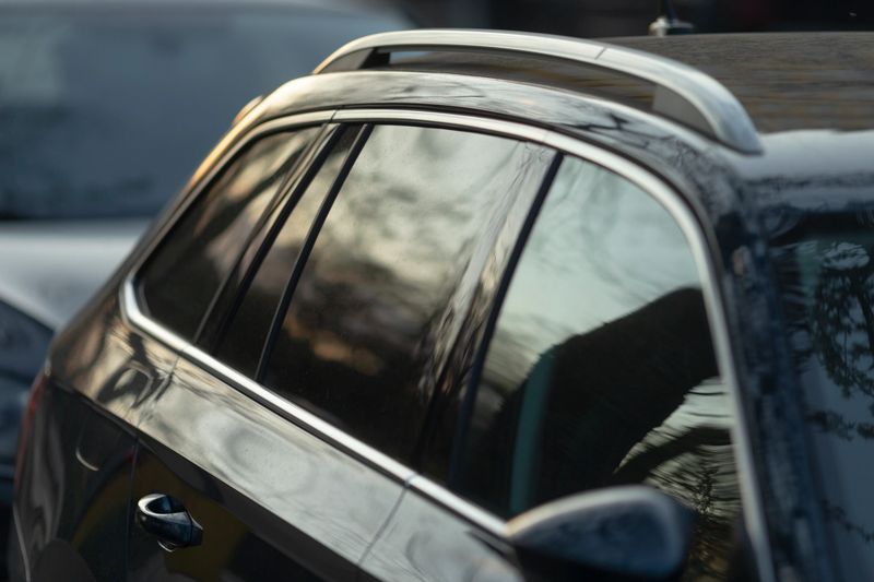 The image beautifully captures a detailed closeup of a cars roof rack, featuring reflective tinted windows that showcase and mirror the surrounding scenery and environment