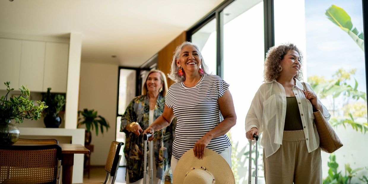 Three women with luggage entering a bright room.