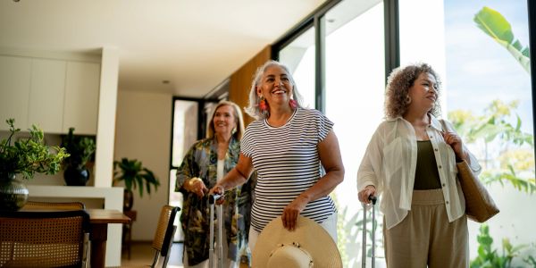 Three women with suitcases entering a room with smiles.