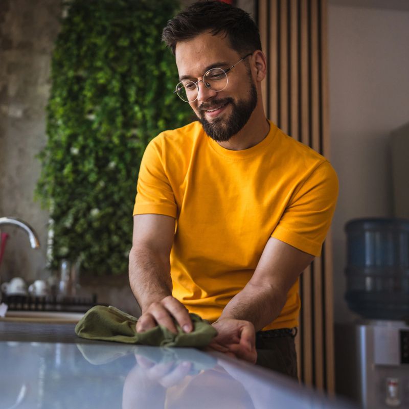 Adult tidy man is wiping and disinfecting a kitchen counter with a rag