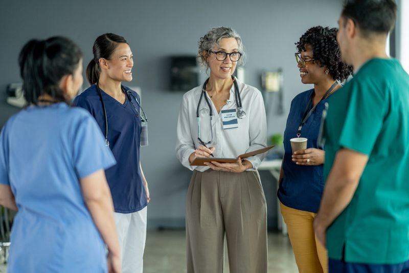 A team of medical professionals wearing uniforms discusses patient care in a hospital environment, exhibiting teamwork, communication, and collaboration critical to providing effective healthcare services.