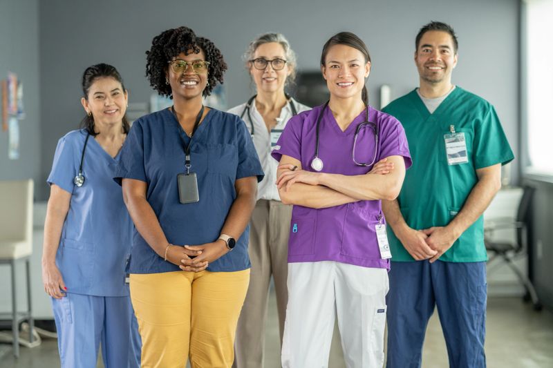 A diverse group of healthcare professionals, including doctors and nurses, smiling confidently in a well-lit clinical setting, symbolizing teamwork, professionalism, and an emphasis on healthcare and diversity.