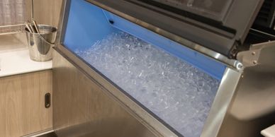 Commercial ice machine filled with ice cubes in a kitchen area.