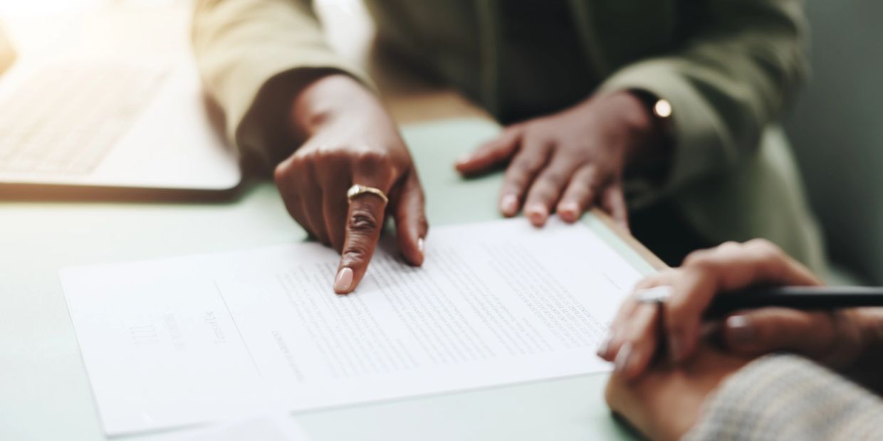 Person pointing at a document while another holds a pen, discussing its contents.