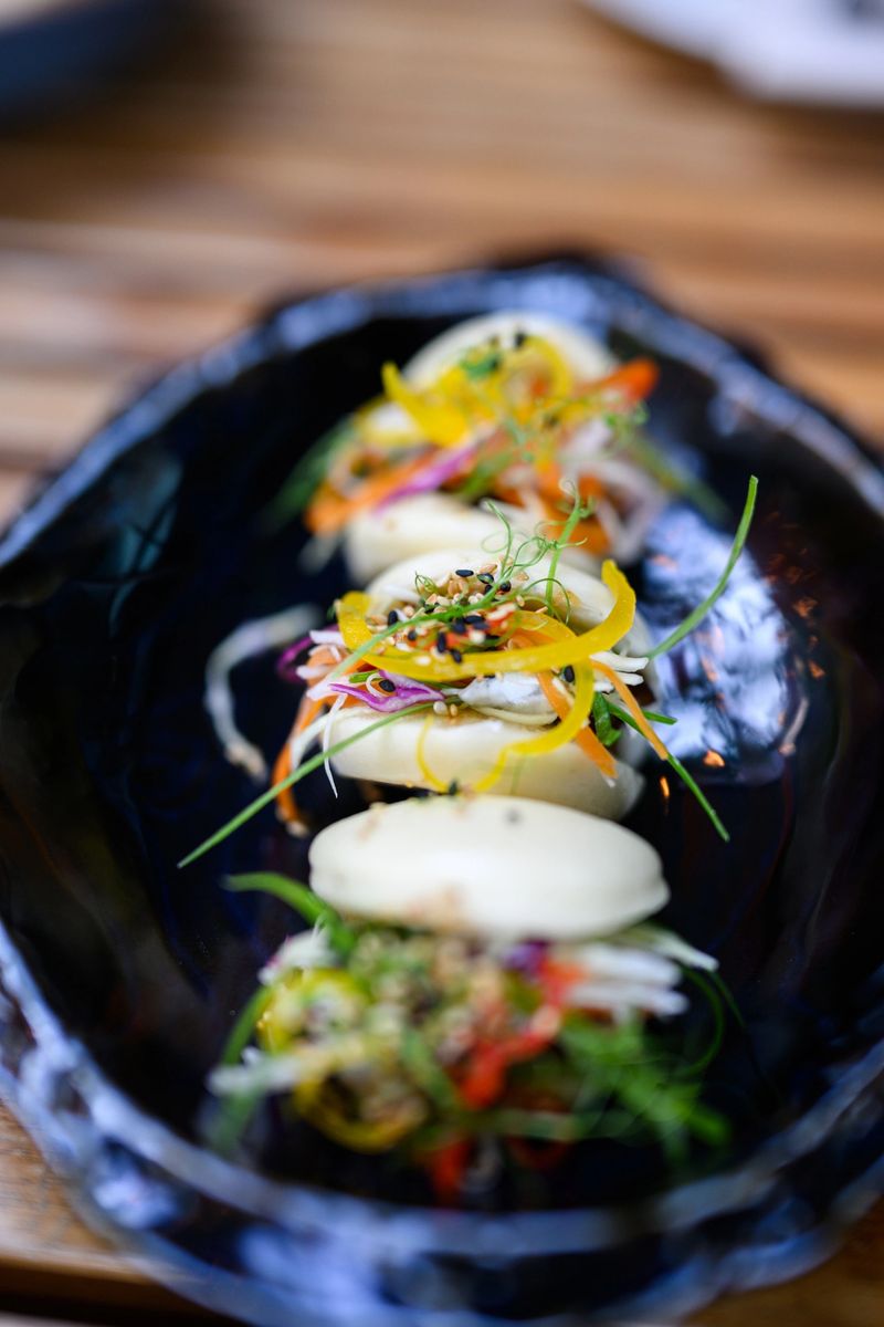 Closeup shot of a steamed buns meal served with colourful vegetables in a black plate, with selective focus.