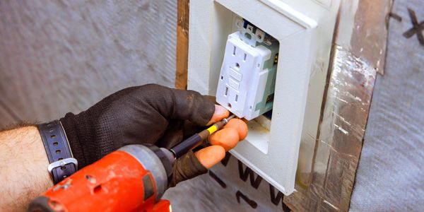 A person installs an electrical outlet using a power screwdriver.