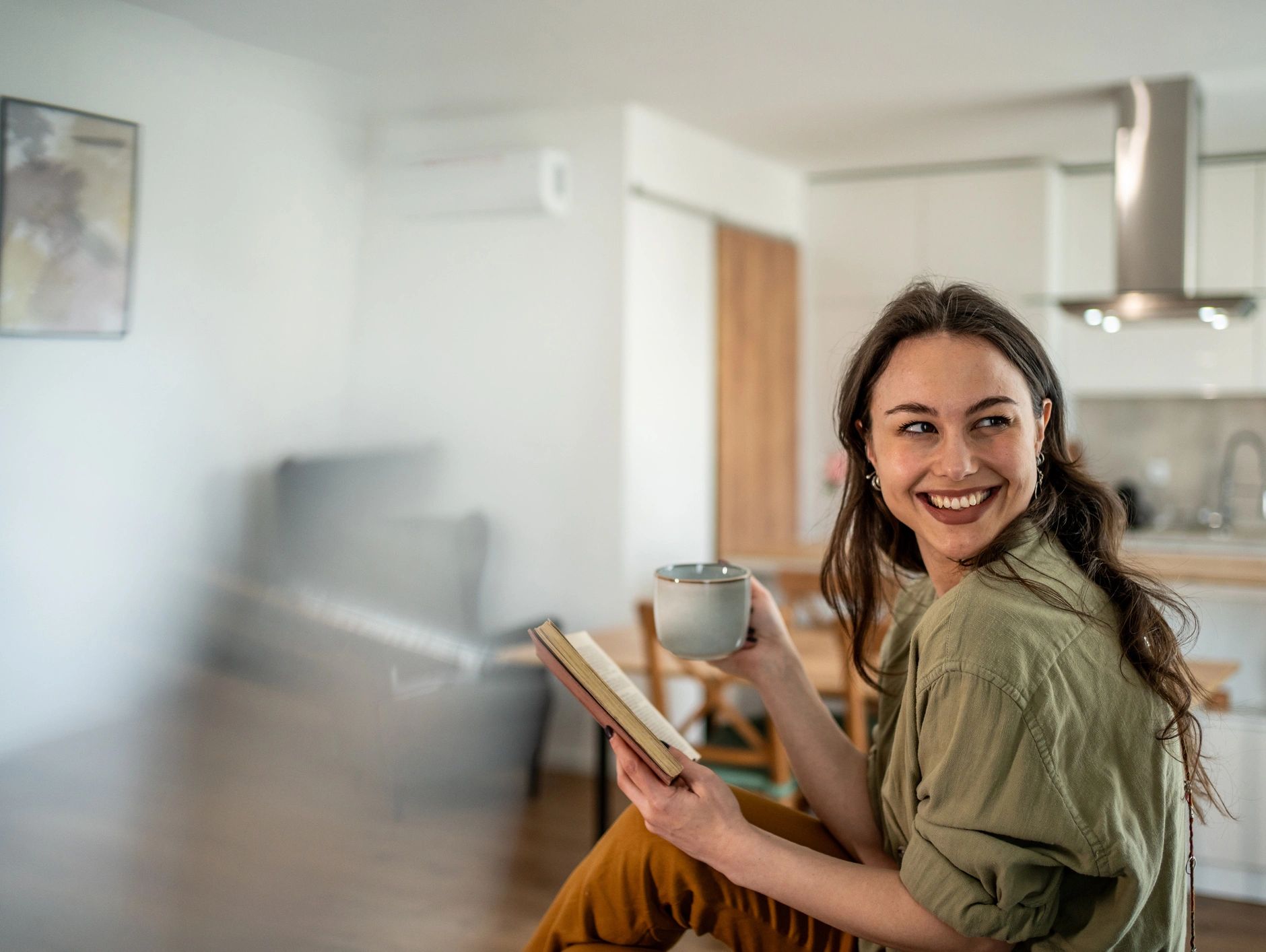 Smiling woman holding a cup and book in a cozy room.