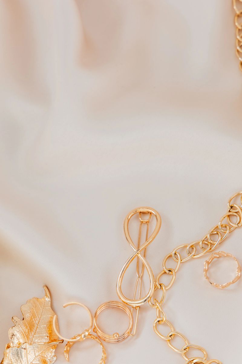 Various pieces of golden jewelry are artistically displayed on a smooth neutral-colored fabric showcasing their intricate designs.