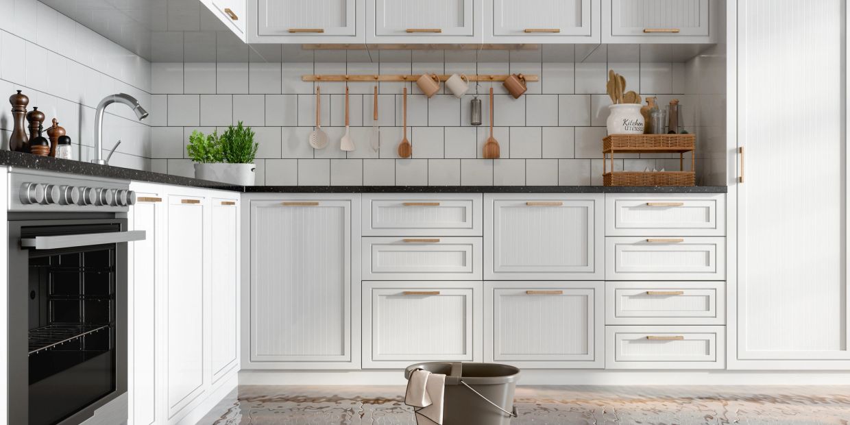 Modern kitchen flooded with water, mop bucket on the floor.