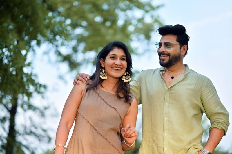 Close-up of a joyful couple walking outdoors, sharing a lighthearted moment. The man has his arm around the woman, and they both smile at each other warmly. Surrounded by greenery and bathed in natural light, the scene captures an affectionate and spontaneous interaction. Ideal for themes of love, happiness, connection, outdoor lifestyle, and romantic relationships.