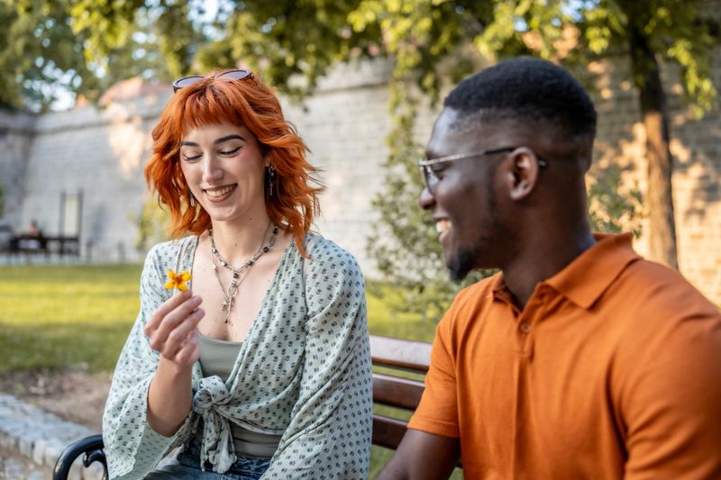 Two friends share a joyful moment seated outdoors on a park bench, surrounded by greenery. Their laughter and smiles create a warm and inviting atmosphere perfect for themes of friendship and happiness.
