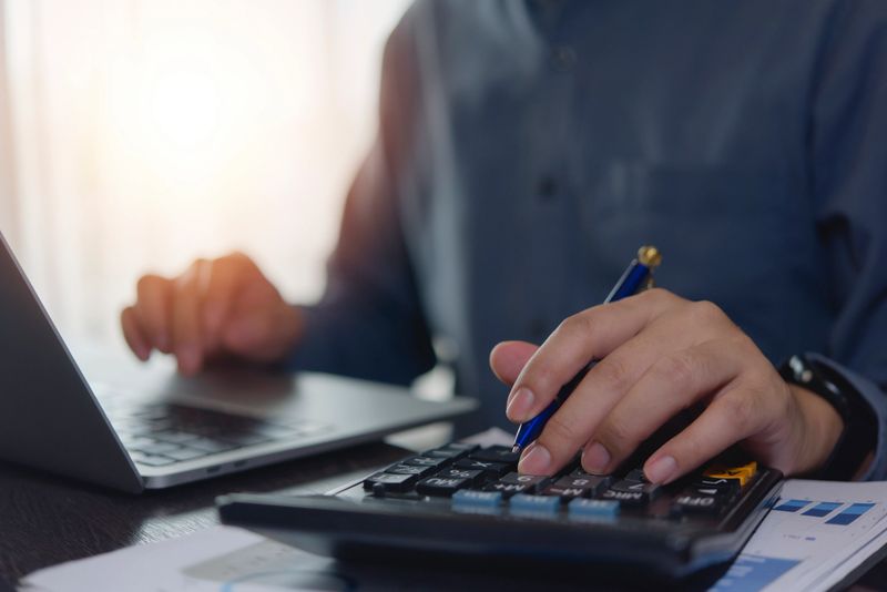 Accountant working hands using calculator and laptop. business finance planning at desk with financial tax documents invoice , pen, and technology management payroll online internet banking concept.