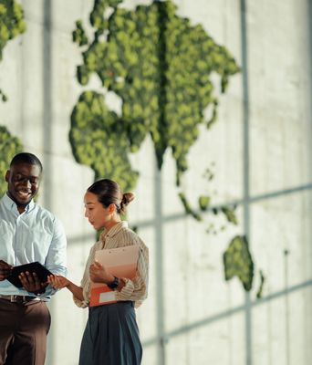 Two professionals discussing work with a leafy world map in the background.