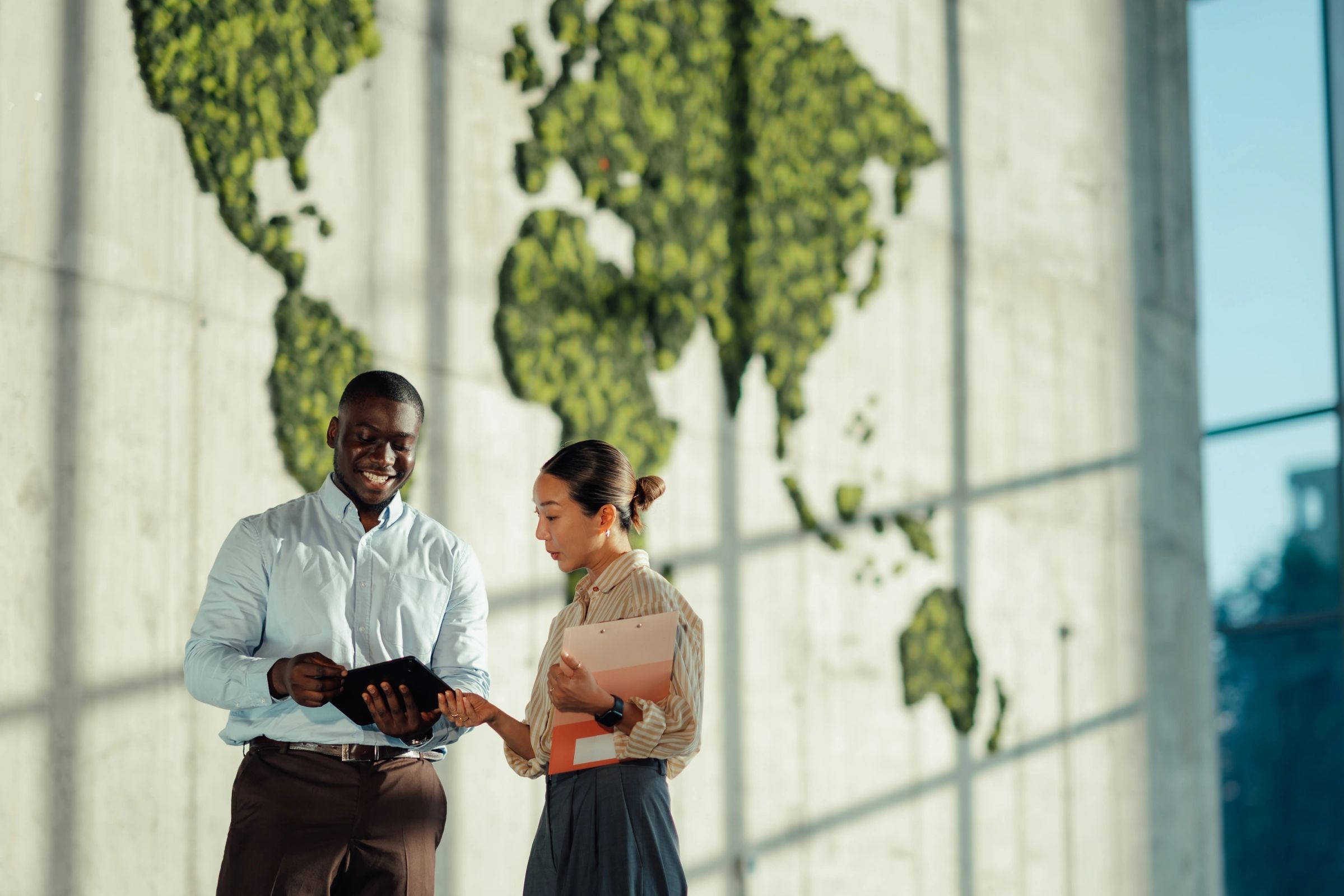 Two colleagues discussing work in front of a green world map on a wall.