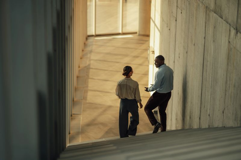 Two businesspeople walking up stairs in a modern office building, engaging in a discussion about their current project and ideas