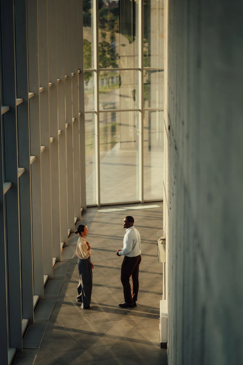 Two businesspeople are having a conversation in the hallway of a modern office building, discussing strategy and planning for future success