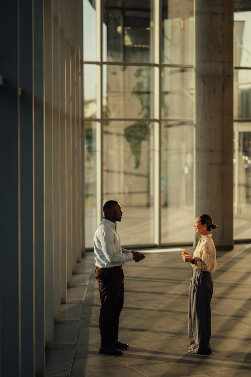 Two businesspeople are discussing work in the lobby of a modern office building with large windows