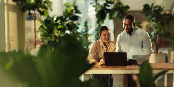 Two colleagues collaborating on a laptop in a lush office environment.